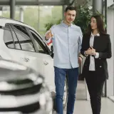 Mężczyzna i kobieta w salonie samochodowym omawiają ofertę wynajem długoterminowy z wykupem.