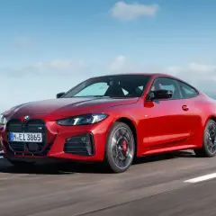 Czerwone coupe BMW M4 na drodze z widokiem na morze i niebo.