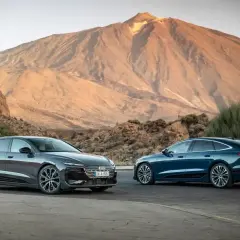 Dwa lśniące Audi, jeden sedan, drugi kombi, na tle majestatycznej góry.
