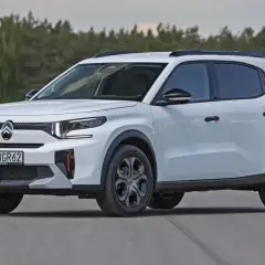 Biały mini suv z czarnymi relingami dachowymi i przyciemnianymi szybami na tle lasu.