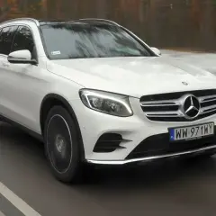 Biały Mercedes GLC 220d z czarnym dachem jedzie po drodze, otoczony zimowym krajobrazem.