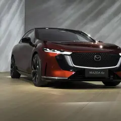 Elegancka, czerwona Mazda 6e prezentuje się na tle nowoczesnej ściany z subtelnymi refleksami światła.