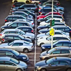Rząd samochodów na parkingu. Znak "Kasse" sugeruje, że to parking płatny. KNF co to? To może być skrót od nazwy firmy zarządzającej parkingiem.