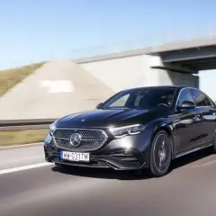 Elegancki, czarny Mercedes E220d mknie autostradą pod betonowym wiaduktem.