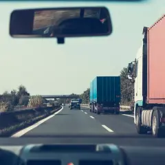 Widok z kabiny samochodu na autostradzie z ciężarówkami i innymi pojazdami.