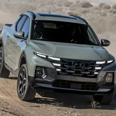 Szary Hyundai Santa Cruz pokonuje pustynny teren, wzbijając tumany kurzu.
