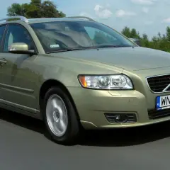 Złoty Volvo V50 2.0D w ruchu drogowym, z zielonymi drzewami w tle.