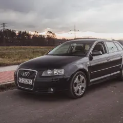Czarne nowe Audi A3 na tle zachodzącego słońca i linii energetycznych.