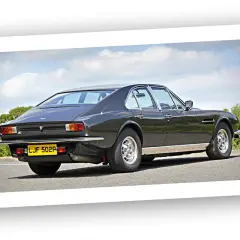 Klasyczny Aston Martin Lagonda z lat 70. na tle błękitnego nieba i zieleni.