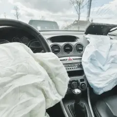 Wnętrze samochodu po wypadku. Rozwinięty **airbag** kierowcy i pasażera, pęknięta przednia szyba.