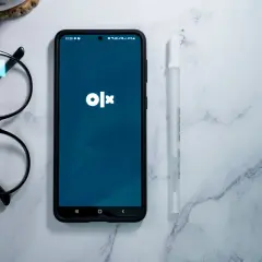 Telefon z aplikacją OLX, okulary i długopis na marmurowym tle. Dowiedz się, jak dodać ogłoszenie na OLX za darmo.