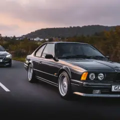 Klasyczne bmw 635 csi i nowszy model jadą drogą o zachodzie słońca.