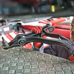 Mechanik w czerwonych rękawiczkach prezentuje element zawieszenia samochodu.