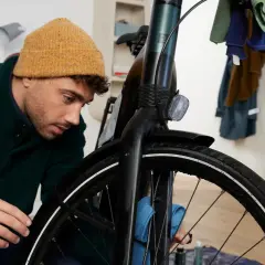 Mężczyzna w czapce czyści rowerową obręcz niebieską ściereczką.