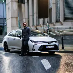 Elegancki mężczyzna opiera się o białą corollę sedan na mokrej ulicy.