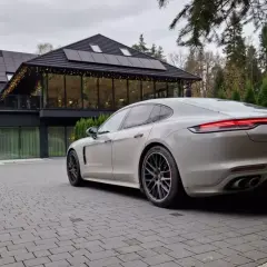 Białe Porsche Panamera GTS przed nowoczesnym budynkiem z panelami słonecznymi. Idealny wybór dla firm ceniących leasing operacyjny.