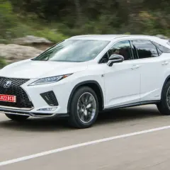 Biały Lexus RX 300 pędzi po krętej drodze wśród zielonych wzgórz.