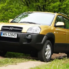 Złoty Hyundai Tucson 2007 na leśnej drodze, gotowy na przygodę.