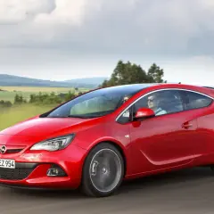 Czerwony Opel Astra J Hatchback pędzi przez malownicze krajobrazy.