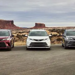 Trzy modele Toyota Sienna 2025 w różnych kolorach stoją na tle pustynnego krajobrazu z formacjami skalnymi.