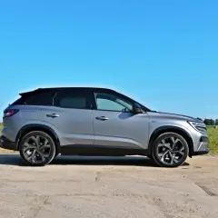Srebrny Renault Austral z czarnym dachem na tle błękitnego nieba i zielonego pola.