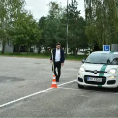 Młody mężczyzna ustawia pachołek na placu manewrowym. Obok stoi biały Fiat Panda z literą "L" na dachu, gotowy do egzaminu.