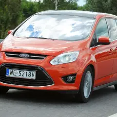 Pomarańczowy Ford C-Max 1.6 TDCI jedzie po drodze, odbijając niebo w szybach.