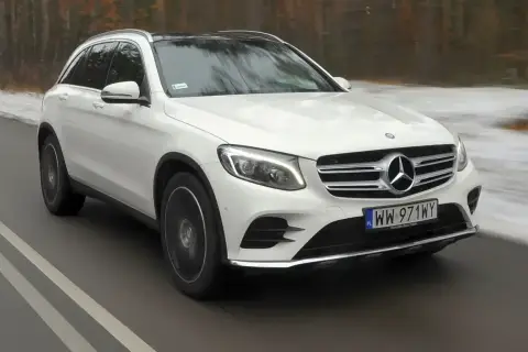 Biały Mercedes GLC 220d z czarnym dachem jedzie po drodze, otoczony zimowym krajobrazem.