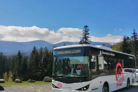 Biały autobus "Karpacz Bus" z napisem "Komunikacja Miejska" na tle gór i lasu. Zastanawiasz się, ile kosztuje autobus?