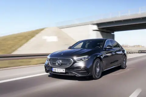 Elegancki, czarny Mercedes E220d mknie autostradą pod betonowym wiaduktem.