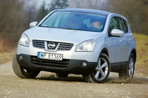 Srebrny Nissan Qashqai 1.6 benzyna pokonuje nierówności na drodze gruntowej, unosząc kurz spod kół.