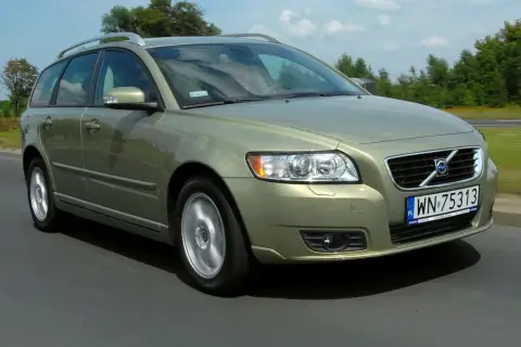 Złoty Volvo V50 2.0D w ruchu drogowym, z zielonymi drzewami w tle.