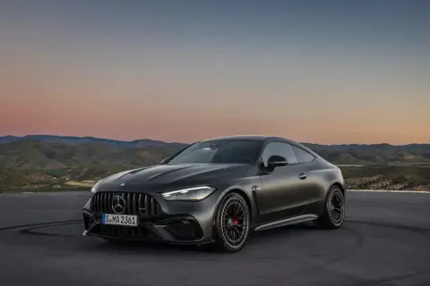 Mroczny Mercedes-AMG GT Coupe na tle zachodzącego słońca i pagórków.