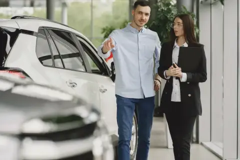 Mężczyzna i kobieta w salonie samochodowym omawiają ofertę wynajem długoterminowy z wykupem.