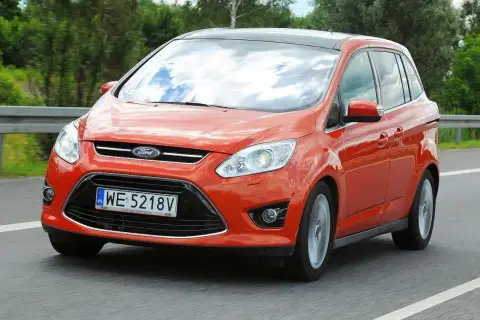 Pomarańczowy Ford C-Max 1.6 TDCI jedzie po drodze, odbijając niebo w szybach.