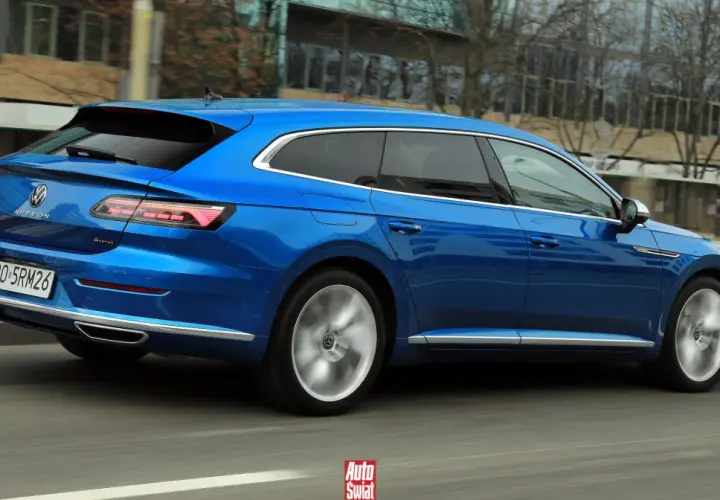 Błękitny Volkswagen Arteon Shooting Brake w ruchu ulicznym. Elegancka linia nadwozia i sportowe felgi podkreślają jego dynamiczny charakter.