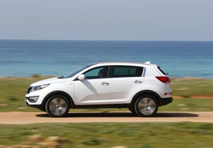 Biały Kia Sportage 2012 jedzie po drodze nad morzem.