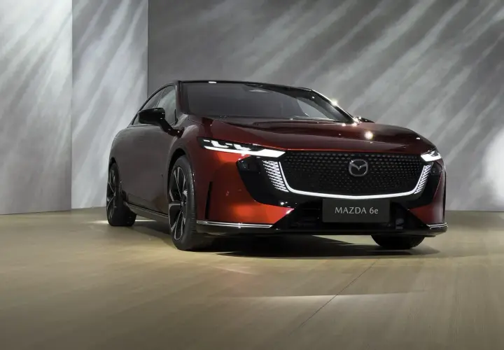 Elegancka, czerwona Mazda 6e prezentuje się na tle nowoczesnej ściany z subtelnymi refleksami światła.
