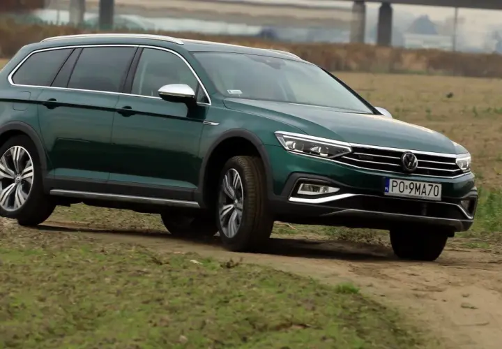 Zielony Passat Alltrack pokonuje piaszczystą drogę wśród traw.