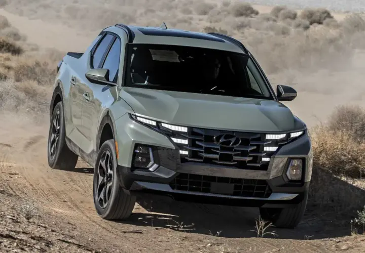 Szary Hyundai Santa Cruz pokonuje pustynny teren, wzbijając tumany kurzu.