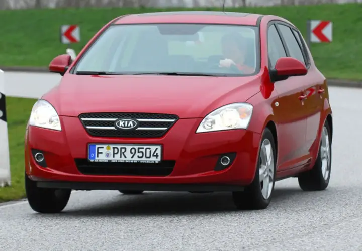 Czerwony Kia Ceed 1.6 CRDi na drodze, z kierowcą za kierownicą.
