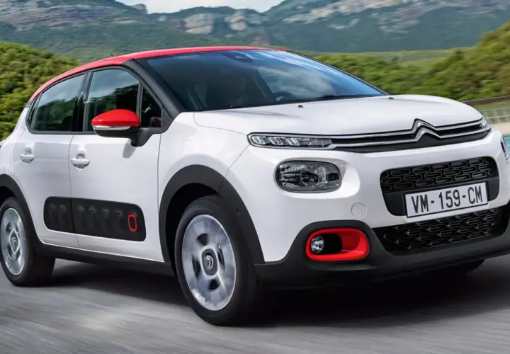 Biały Citroen C3 2025 z czerwonym dachem i lusterkami jedzie po drodze, otoczony zielonymi wzgórzami.