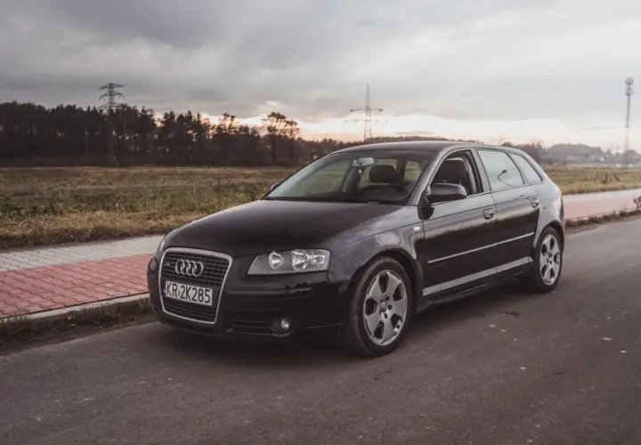 Czarne nowe Audi A3 na tle zachodzącego słońca i linii energetycznych.