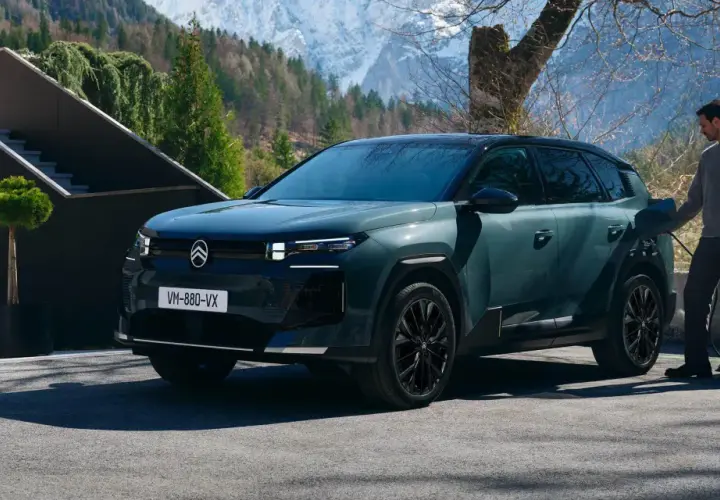 Nowy Citroën C5 Aircross 2025, zielony SUV, ładowany przy górskim domu. Kobieta w płaszczu wychodzi z budynku.