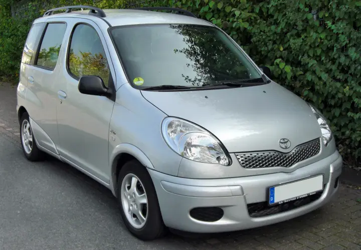 Srebrny Toyota Yaris Verso stoi na tle zielonych krzewów.