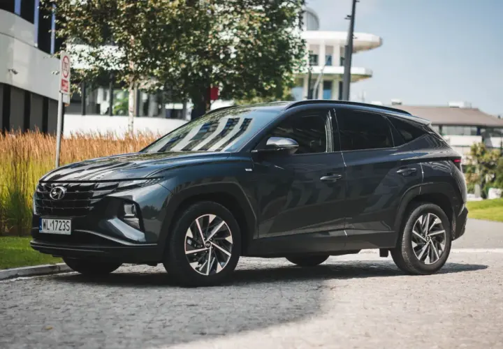 Ciemnoszary Hyundai Tucson 2020 zaparkowany na brukowanej ulicy, z nowoczesnym budynkiem w tle.