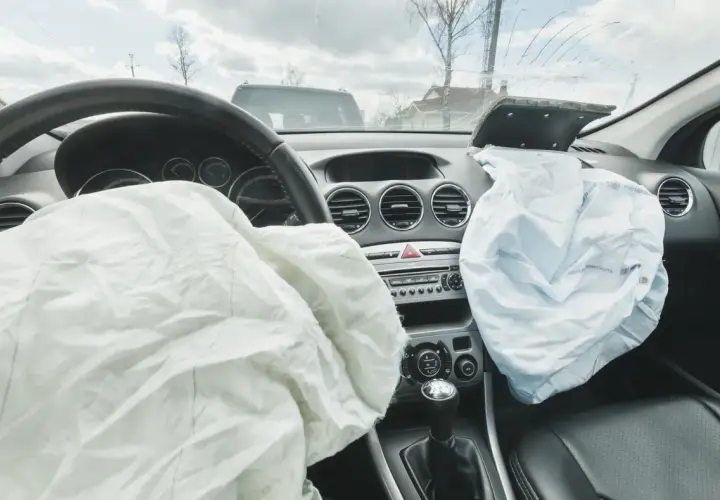Wnętrze samochodu po wypadku. Rozwinięty **airbag** kierowcy i pasażera, pęknięta przednia szyba.