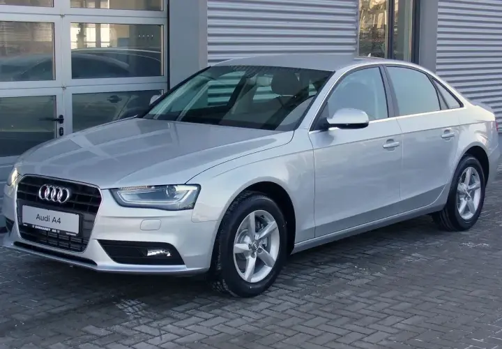 Srebrny Audi A4 B8, model znany z typowych usterek, stoi przed budynkiem.