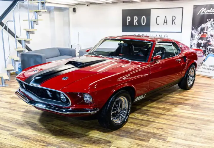 Błyszczący czerwony Ford Mustang Mach 1 z 1969 roku z czarnymi pasami na masce, gotowy do jazdy.