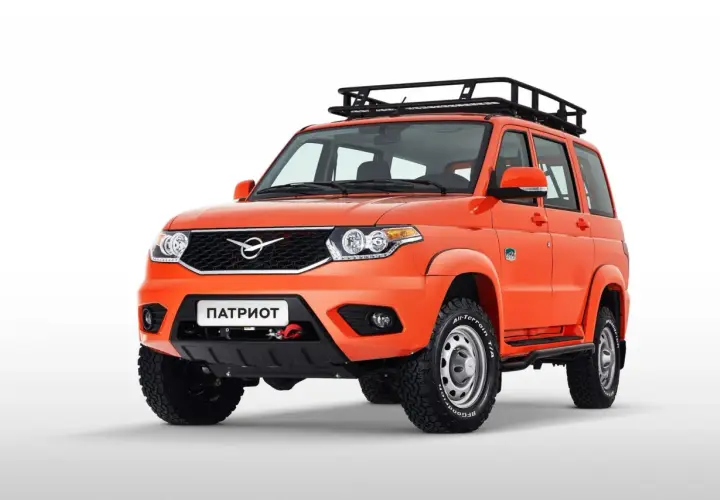 Pomarańczowy UAZ Patriot z bagażnikiem dachowym i wyciągarką na białym tle.